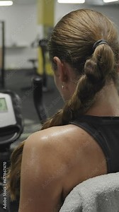 Vertical video. Woman in the Gym on a Stationary Bike, Pedaling, and Her Back Covered in Sweat Droplets. Fat-Burning and Invigorating Workout!