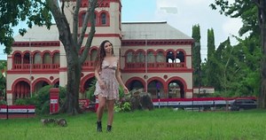 A young woman spins and dance in a mini dress at a park with a castle in the background