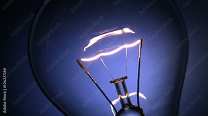 Close up of the filament of an electric light bulb glowing on and off. Blue background.