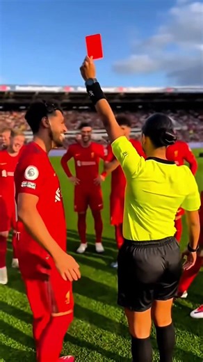 female referee halts the match and firmly raises a red card toward a male player