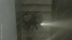 Men with rifles and flashlights climbing ladder. Long shot of armed men slowly moving forward, covering and defending each other, playing airsoft in building. Game, entertainment concept Stock Video