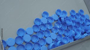 Many blue plastic bottle caps moving on conveyor belt of automatic compression molding machine at factory, exhibition: production line. Manufacturing, industry, recycling, technology equipment concept