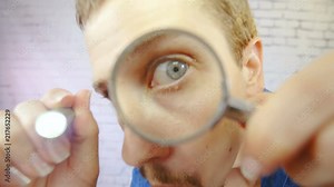 Man with magnifying glass and flashlight look into camera lens 4K. Portrait wide lens with a person face in focus while pushing a magnifying glass into camera lens.
