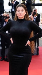 The woman in the image is **Ilfenesh Hadera**, an American actress known for roles in shows like *Godfather of Harlem* and films like *Baywatch*. She wore this stunning form-fitting black gown — a long-sleeved, high-neck design with subtle sparkling polka-dot embellishments — on the red carpet at the **78th Cannes Film Festival in 2025**, specifically for the premiere of the film *Highest 2 Lowest*. The confident hands-on-hips pose and the classic Cannes backdrop with photographers perfectly cap