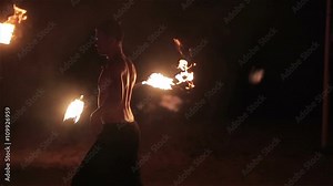 Fire show performance. Handsome male fire performer twirling and tossing up fire baton staff ignited from both sides. Slow motion