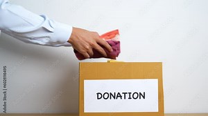 Donation, Charity, Volunteer, Giving and Delivery Concept. Hand holding Clothes into Donation box at home or office for support and help poor, refugee and homeless people. Copy space for text
