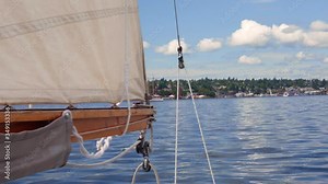 Sailboat boom drifts back and forth in the slow wind. The pulleys in the shot sway and move with the wind and sail. The mast is made of wood. You can see the Seattle in the background behind the sail.