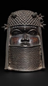 Possibly over 500 years old, this Commemorative Head (uhunmwun-elao) is attributed to the Ẹdo peoples of the Benin Kingdom in present-day Nigeria. It is made of copper alloy and iron and features an Ọba wearing layered coral bead necklaces, a netted cap with tubular beads, and slender braids alongside the temples. The thickly cast head is believed to have once supported a tusk. It measures 29.9 × 21.6 × 20.4 cm (11 3/4 × 8 1/2 × 8 1/16 in). This artifact is now housed at the Cleveland Museum of 