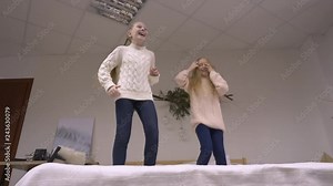 Happy girls jumping on bed. Bottom view two playful little girls jumping on bed. Teenage girls having fun in the bedroom. Slow Motion low angle