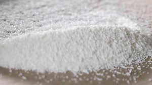 White plastic polymer granules spread and leveled with a wooden stick on cardboard, Close-up of raw material handling for plastic production or injection molding