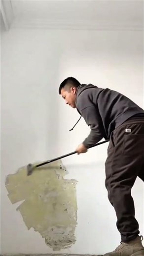 Scraping off the old paint from the wall surface using a long handled metal scraper tool manually