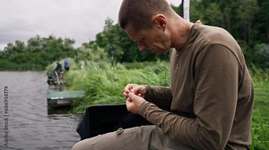 Close-up male fisherman's hand stringing bait onto the hook of a fishing rod for catching river fish