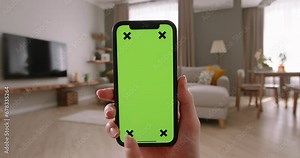Captured up close, woman's right hand with smartphone featuring chroma key screen mock-up in living room. Tap at bottom of screen, buy online, submit application, interact with phone app, advertising