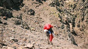 A climber with a large backpack with equipment descends from the mountain on a rope using a belay system. The tourist descends the rope with the help of the "figure eight" descent device