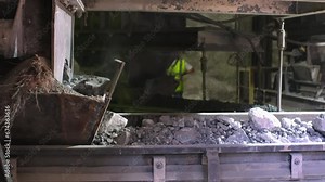 Cement factory. A conveyor with stones and gravel undergoes the crushing process. Modern technologies at a cement plant. Technological work for cement production. Close-up of raw material grinding.