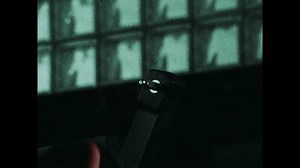 UNITED STATES 1970s: A close-up of a hand operating a vintage film projector, focusing on the reel and mechanical components. The lighting is dim, highlighting the intricate details of the projector.