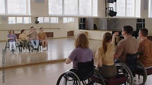 Arc shot of wheelchair dance team and professional choreographers learning new moves in front of mirror wall in studio, then laughing together while having fun on rehearsal