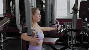 Athletic woman with a beautiful figure trains pectoral muscles on the simulator in the gym.