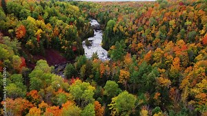 Beautiful panning out aerial flying above the Potato River and colorful fall tree foliage with a view looking towards Lower and Upper Potato River Falls waterfall cascades and red dirt sloped cliffs.