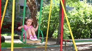 Little girl in a pink dress with dots is sitting on the swing.