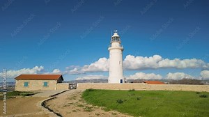 old lighthouse in Pafos, Cyprus, standing tall against a striking blue sky dotted with fluffy clouds. Historic lighthouse serves as a maritime beacon and a popular landmark for its panoramic views