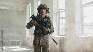 Beautiful young adult fully equipped woman soldier holding rifle gun standing in place of battle in damaged building looking at camera. War in Ukraine. Armed conflict. Female amy officer in war zone