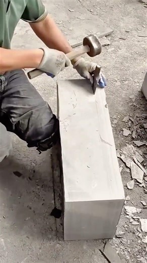 splitting large grey stone blocks with precision tools in an open outdoor construction workshop area