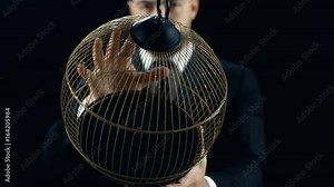 Professional Magician in a Black Suit Performs Bird (White Parrot) Appearing in an Empty Cage Trick. The Background is Black. Shot on RED EPIC-W 8K Helium Cinema Camera.