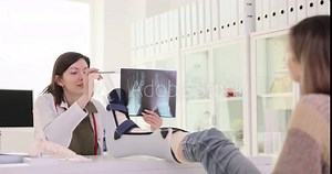 Doctor traumatologist showing xray of bones of feet to patient with broken leg in bandage 4k movie slow motion. Treatment and diagnosis of limb fractures concept