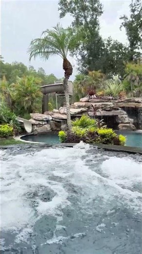 This backyard has a huge grotto, a waterslide, a big elevated spa with a swim-up bar, a sun shelf