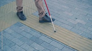 Visually impaired man is walking on a tactile warning tile with the help of his cane. Detectable warning surface for the vision impaired outdoors in the city.