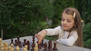 Close up cute little girl playing chess outdoor. Concentrated smart child chess player making a chess move in educational board game. Kid development, gain abstract thinking skills, hobby concept
