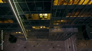 Top view of Modern skyscraper with glass surface in late evening. Skyscraper facade with illuminated offices, drone shot moving backwards and panorama revealing the building.