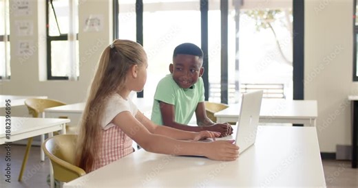 Diverse school-age classmates working on laptop in class for task girl pointing guiding boy typing