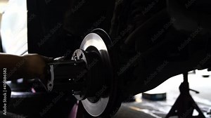 Cleaning disc brake. A car mechanic repairing the brakes. Mechanic examining car wheel brake disc of lifted automobile at repair service station.