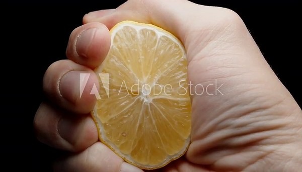 I squeeze the juice from half a lemon. Slow-motion view from below, drops appear to be flying towards you. Close-up.