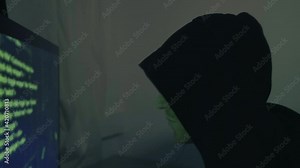 Hacker in front of his computer screen coding and hacking into security systems in dark green room. Hooded guy cyber-attacking an online system breaking into the internet network. Man programming code