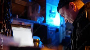 Adult brutal man smokes vape cigarette and works at laptop at dark room with neon light