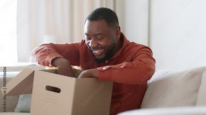 Unpacking concept. Excited african american guy opening delivery box and getting purchase, tracking shot, free space