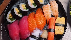 Assorted sushi platter with various types of nigiri, maki rolls, and sashimi on black plate, showcasing Japanese cuisine. Authentic Japanese Food and Culinary Arts.