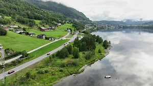 Bus and cars on road E16 to Voss Norway - Aerial following traffic from side before ascending above road to reveal panoramic view of Voss and crystal clear Vangsvatnet lake