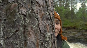 Woman playing and hiding behind a tree in a forest in slow motion.