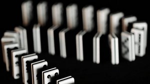 Falling dominoes in slow motion, creating a chain reaction effect on a black background. A perfect 4K footage for concepts like cause and effect, risk, failure, leadership and decision-making.