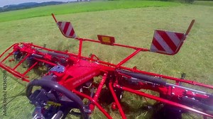 Rotary rakes are moving very fast to turn the dry grass around. It is a hot summer day in the field. Wide-angle shot.