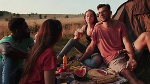 True four young friends having a pleasant conversation while camping outdoors in bright sunlight, enjoying cocktails and laughing. Tourism concept, real friendship, active lifestyle