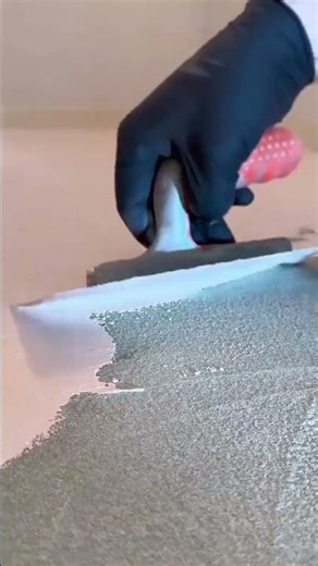 Spreading a thick layer of white plaster over a textured green surface using a metal hand trowel