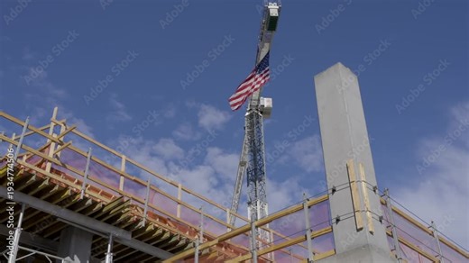 This video shows a large American flag blowing in the wind in slow motion on an industrial crane.