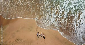 Group of friends people enjoying the beach laying on the sand - aerial top view with waves comnig, summer vacation travel lifestyle for young men and women during holiday - coloured landscape from ver Stock Video