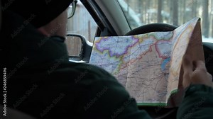 In winter a man sits in a car and studies the navigation map. Man runs his finger on navigation map.