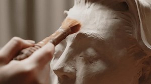 Close up of unrecognizable sculptor cleaning clay bust of young woman with brush while crafting in workshop